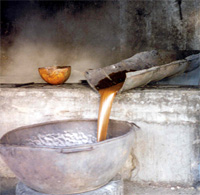 Sugar cane juice running down a wooden trough into a large metal boiling pan