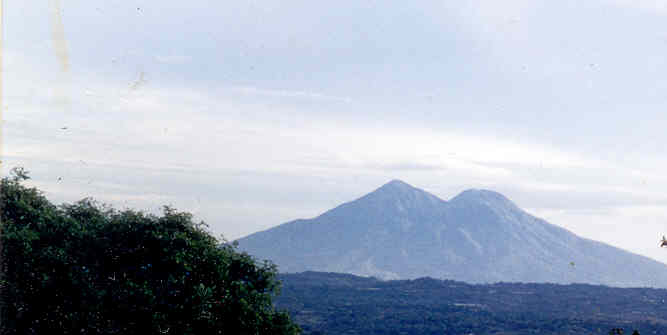The twin peaks of the San Vicente volcano rising beyond wooded hills